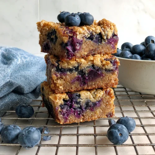 Delicious Blueberry Baked Oatmeal That Everyone Will Love 1 Blueberry baked oatmeal bars stacked with blueberries.