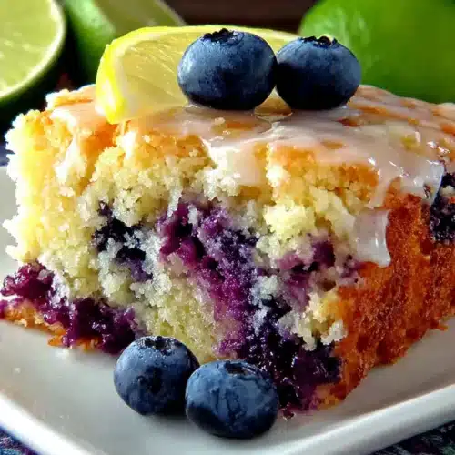 A slice of blueberry boyfriend bait cake with fresh blueberries and lemon glaze on a white plate