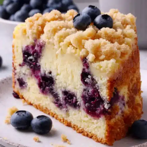Slice of blueberry crumb cake with crumb topping and fresh blueberries