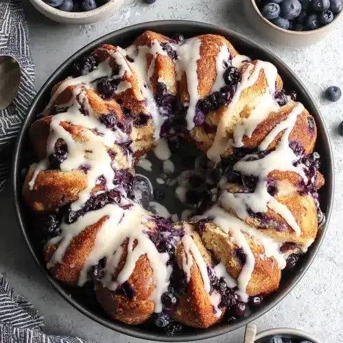 Delicious Blueberry Monkey Bread Recipe for Family Fun 1 Blueberry monkey bread with white glaze and fresh blueberries on a plate