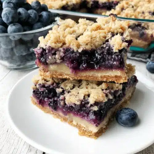 Delicious Blueberry Oat Crumble Bars: A Healthier Delight 1 Blueberry oat crumble bars stacked on a white plate with fresh blueberries nearby.