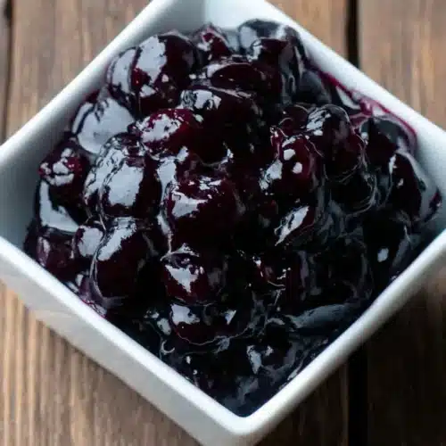 Quick and Easy Blueberry Sauce Recipe That Everyone Will Love 1 Glossy blueberry sauce in a white bowl on a wooden surface