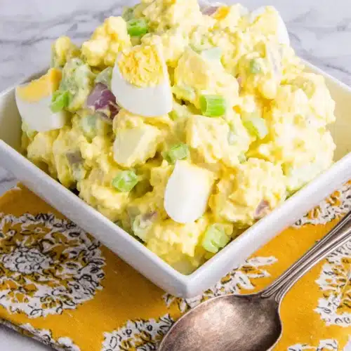 Classic Potato Salad: A Deliciously Simple Side 1 Classic potato salad in a white bowl with a spoon, served on a yellow napkin
