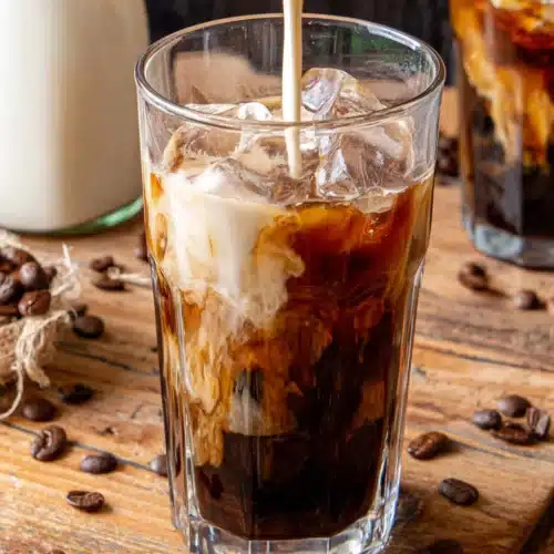 Delicious Cold Brew Coffee Recipes to Refresh Your Day 1 Cold brew coffee with cream and ice in a glass, surrounded by coffee beans