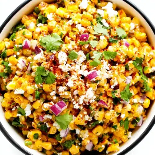 Easy Elote Dip: A Flavorful, Family-Friendly Snack 1 Easy elote dip in a white bowl with black rim, topped with cheese, cilantro, and chili powder.