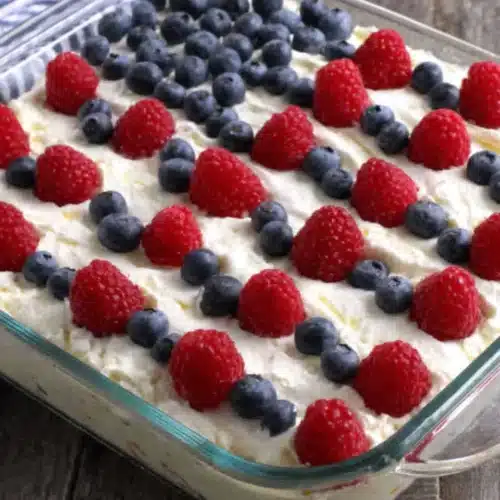 Easy flag cake with red raspberries and blueberries arranged in an American flag design on white whipped topping