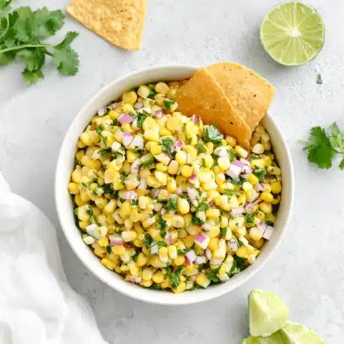 Corn Salsa: A Colorful and Easy Delight 1 Fresh corn salsa in a white bowl with tortilla chips, lime, and cilantro
