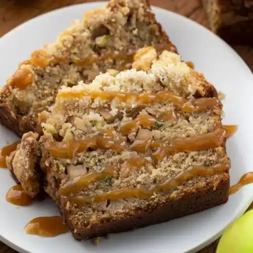 Delicious Apple Zucchini Bread Recipe That Everyone Loves 2 Slices of apple zucchini bread with caramel drizzle and crumb topping on a white plate