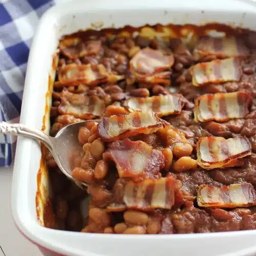 Backyard barbecue baked beans with bacon in a white dish, topped with crispy bacon