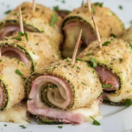 Baked Zucchini Rolls with Cheese: A Delightful Treat 2 Baked zucchini rolls with cheese, ham, and herbs on a white plate