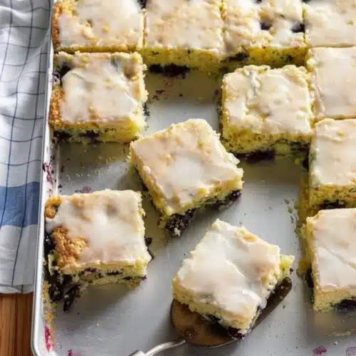Delicious Blueberry Zucchini Bars for Your Family 2 Blueberry zucchini bars with white icing on a baking sheet, some cut and served.