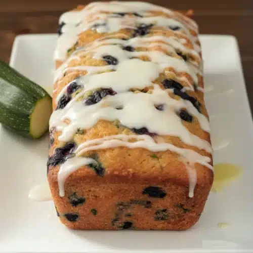 Delicious Blueberry Zucchini Bread with Lemon Glaze 2 Blueberry zucchini bread with lemon glaze on a white plate, fresh blueberries and zucchini nearby