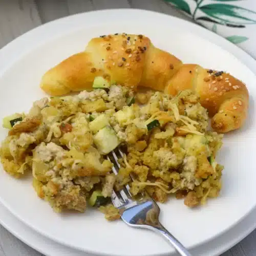 Delicious Chicken Zucchini & Stuffing Mix Casserole 2 Chicken zucchini stuffing mix casserole served on a white plate with a croissant and fork