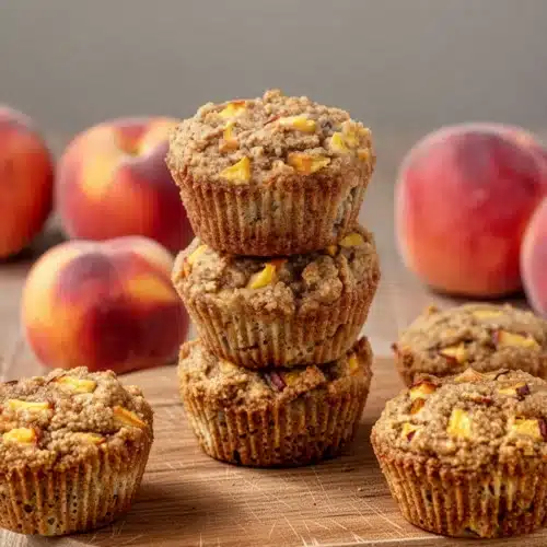 Delicious Gluten-Free Peach Muffins for Everyone 2 Gluten-free peach muffins stacked with fresh peaches in background