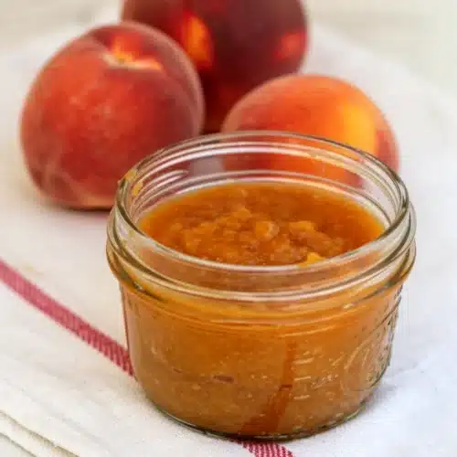 Old-Fashioned Peach Butter: A Delightful, Easy Spread 2 Old-fashioned peach butter in a glass jar with fresh peaches on a striped cloth