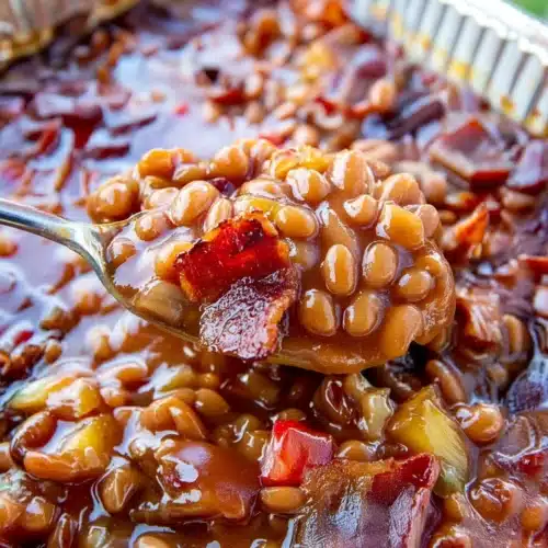 Delicious Smoked Baked Beans - A Must-Try Recipe! 1 Smoked baked beans with bacon and pineapple in a foil pan, spoon lifting a scoop