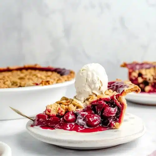 Tart Cherry Pie: A Delightfully Sweet Indulgence 1 A slice of tart cherry pie topped with vanilla ice cream, served on a white plate.