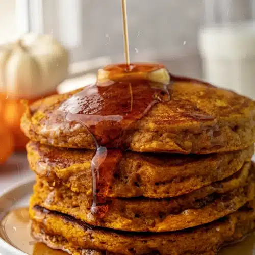 Stack of baked pumpkin pancakes with maple syrup and butter