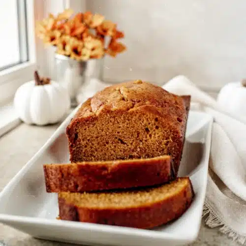 Moist pumpkin bread slices on a white plate with fall decor, best pumpkin bread recipe easy